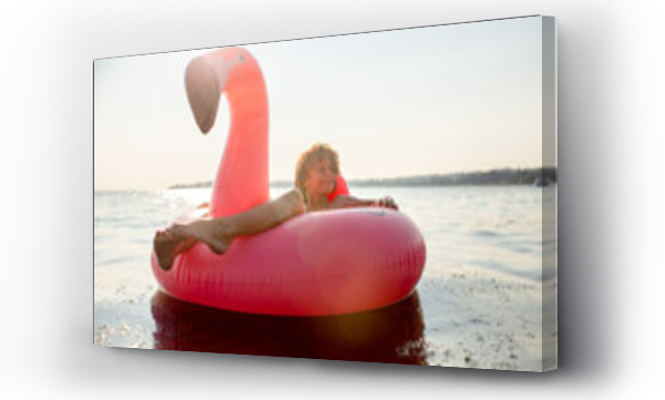 Uśmiechnięty chłopiec pływa spokojnie w różowym flamingo floatie